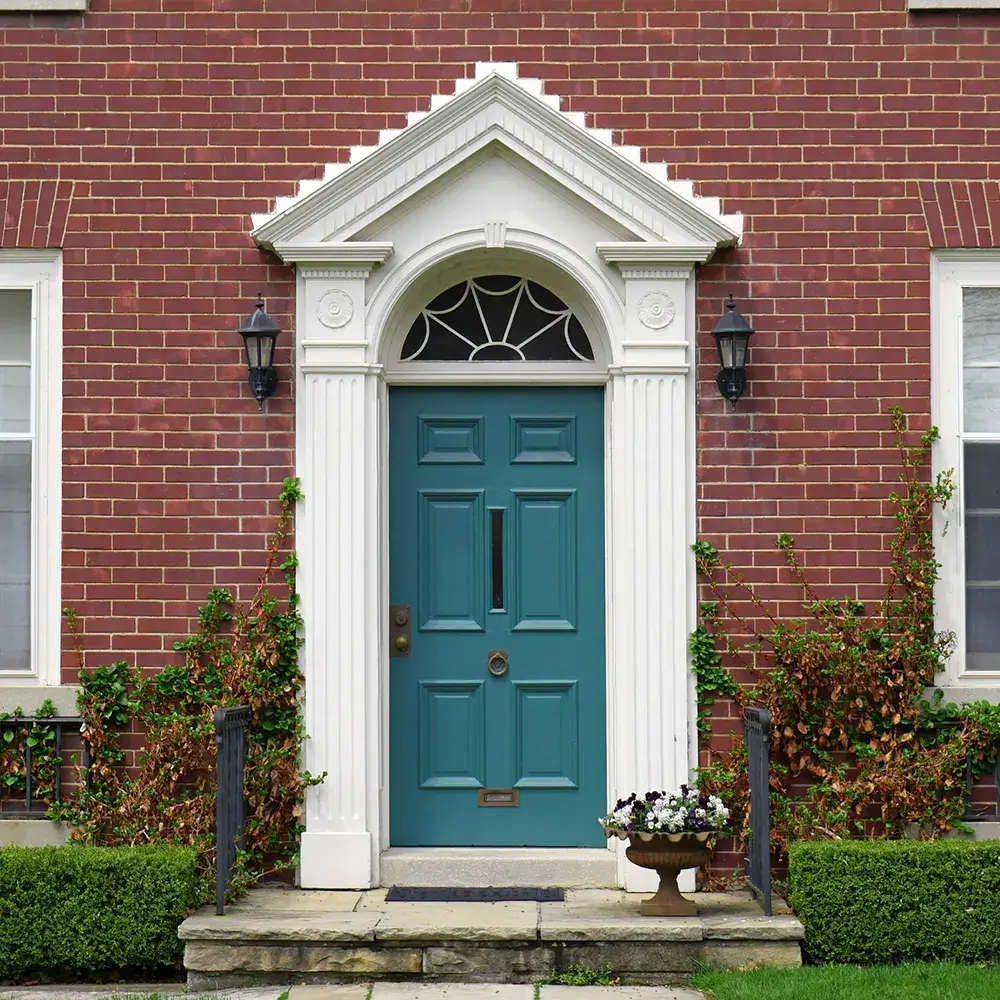 Elegant teal front door with white columns and arched transom on red brick home