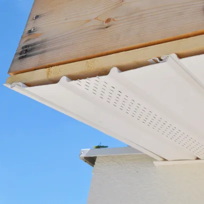 White perforated vinyl soffit installation under wooden roof eaves against blue sky
