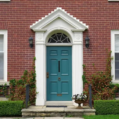 Elegant teal front door with white columns and arched transom on red brick home