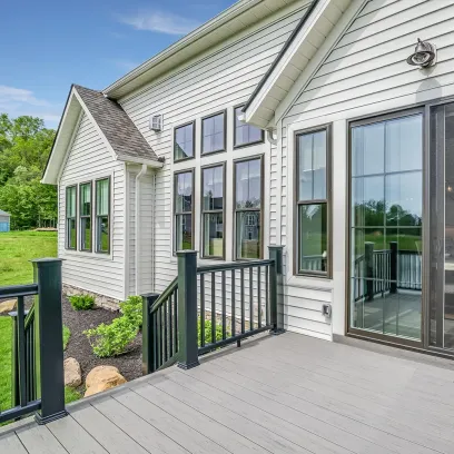 Modern beige vinyl siding house with large windows and wooden deck with black railings
